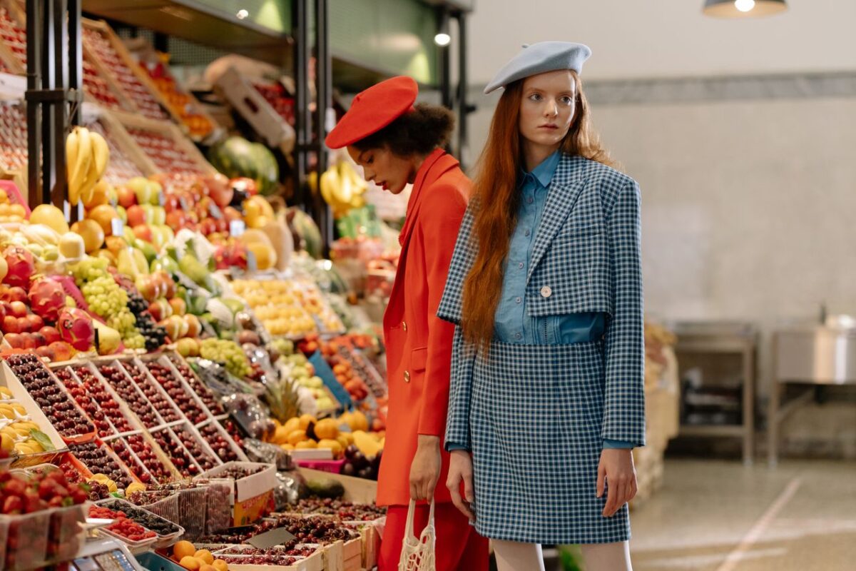 Stylishly dressed women browsing a vibrant indoor fruit market display.